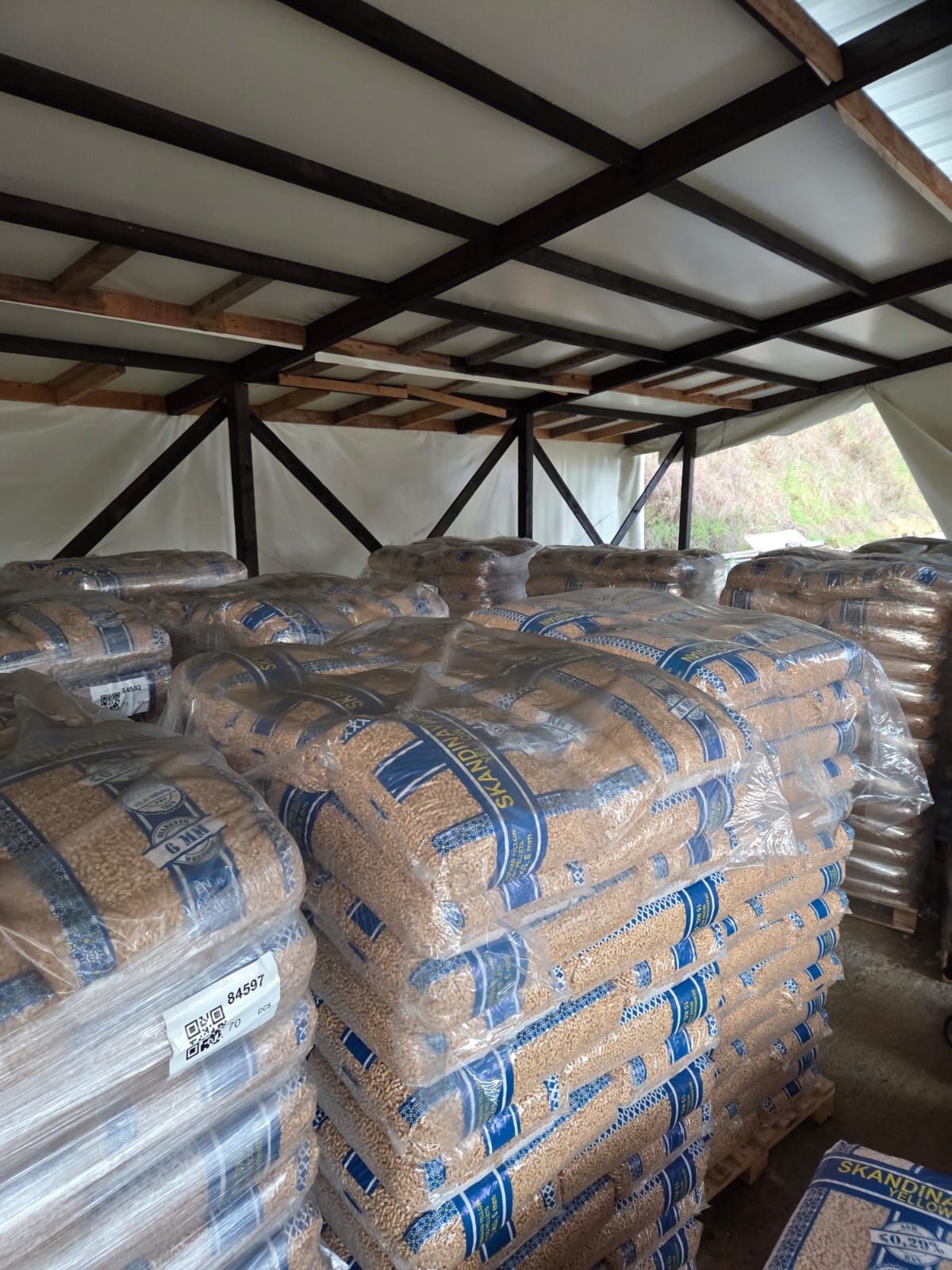 Sacchi di pellet di legno accatastati in una struttura di stoccaggio, sotto un tetto di legno.