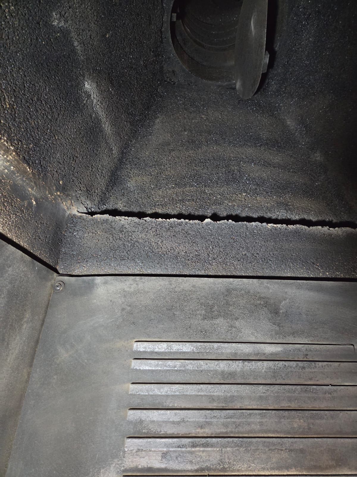 Vista interna di un camino rettangolare scuro. Una crepa orizzontale attraversa la parete posteriore superiore, ruvida.