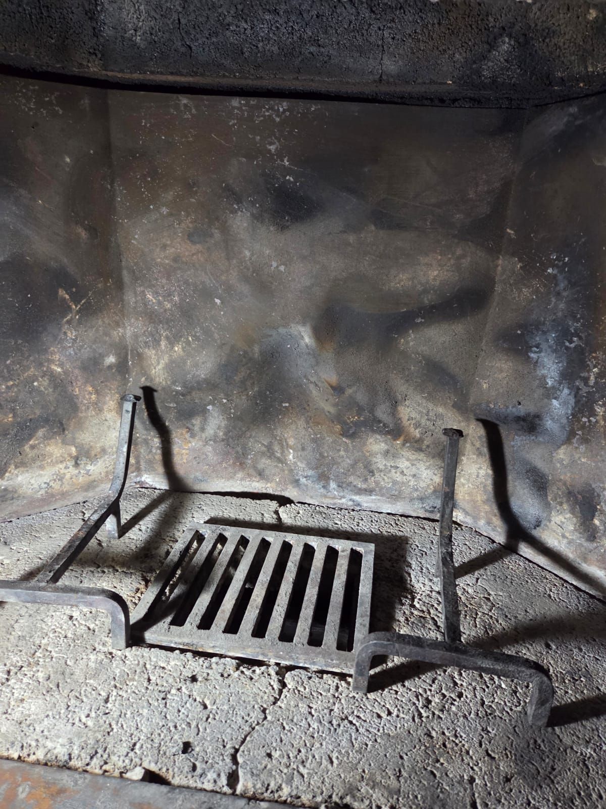 Interno del camino con griglia e cenere; le pareti sono macchiate di fuliggine grigia e nera.
