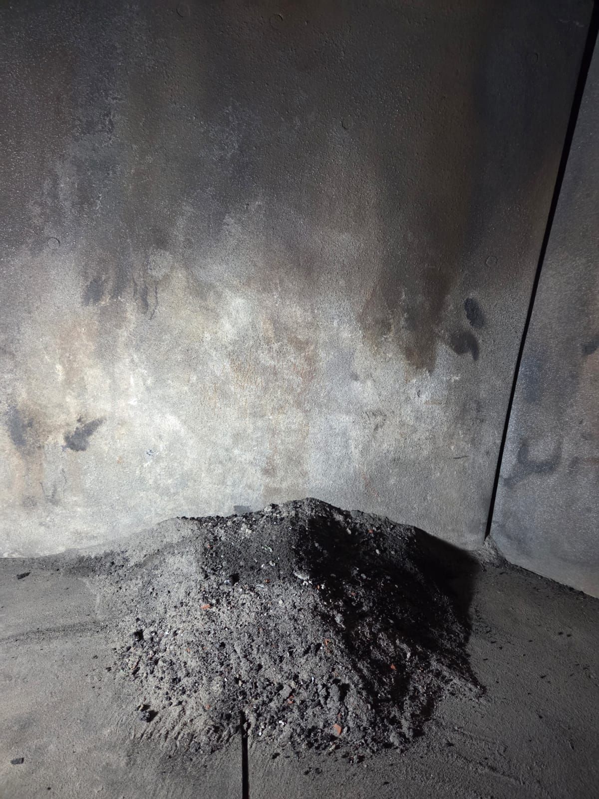 Mucchio di cenere in un camino buio e fuligginoso, con residui sulle pareti.
