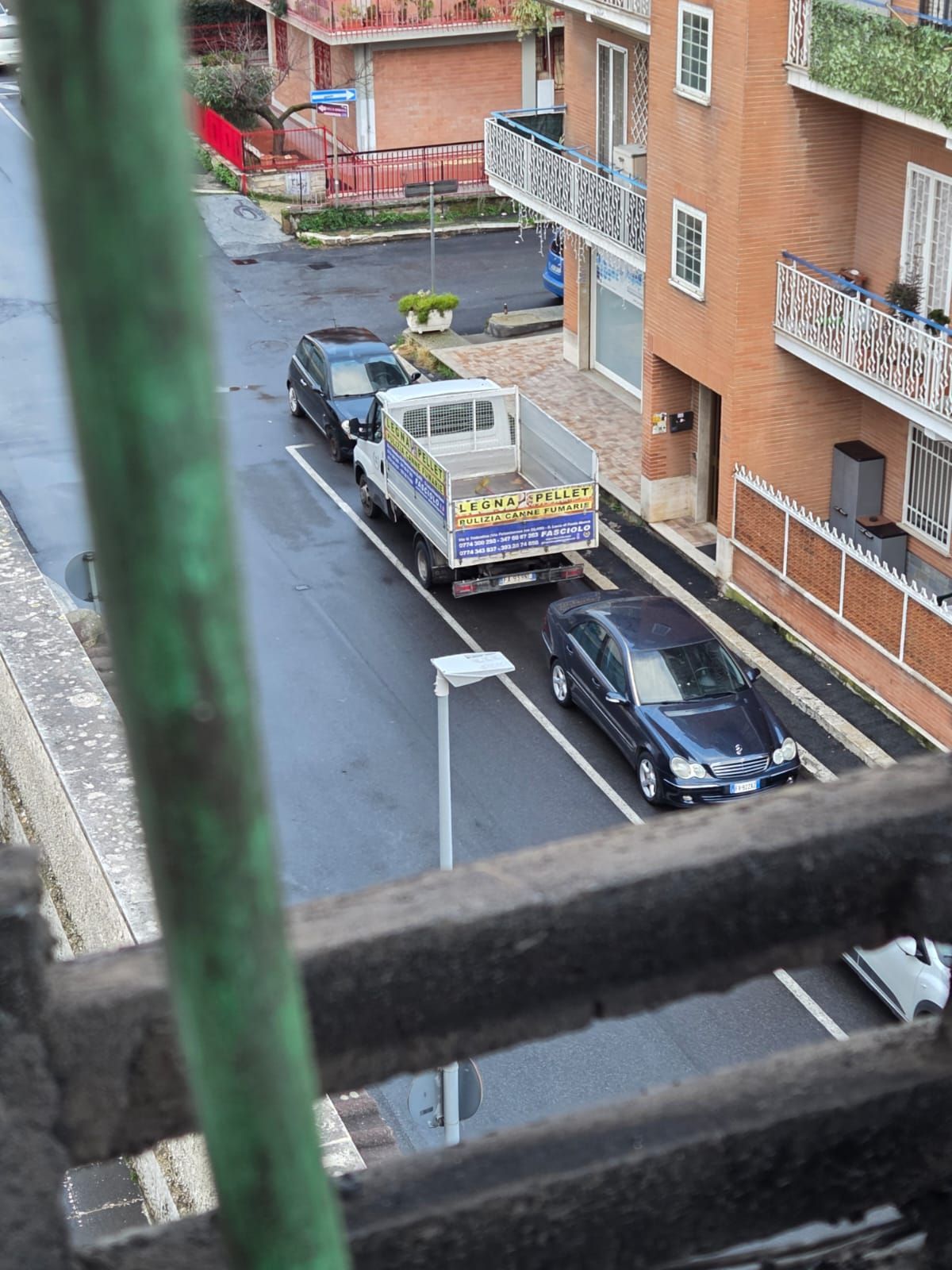 Vista di una strada con un camion e delle auto. Edifici con balconi costeggiano la strada.