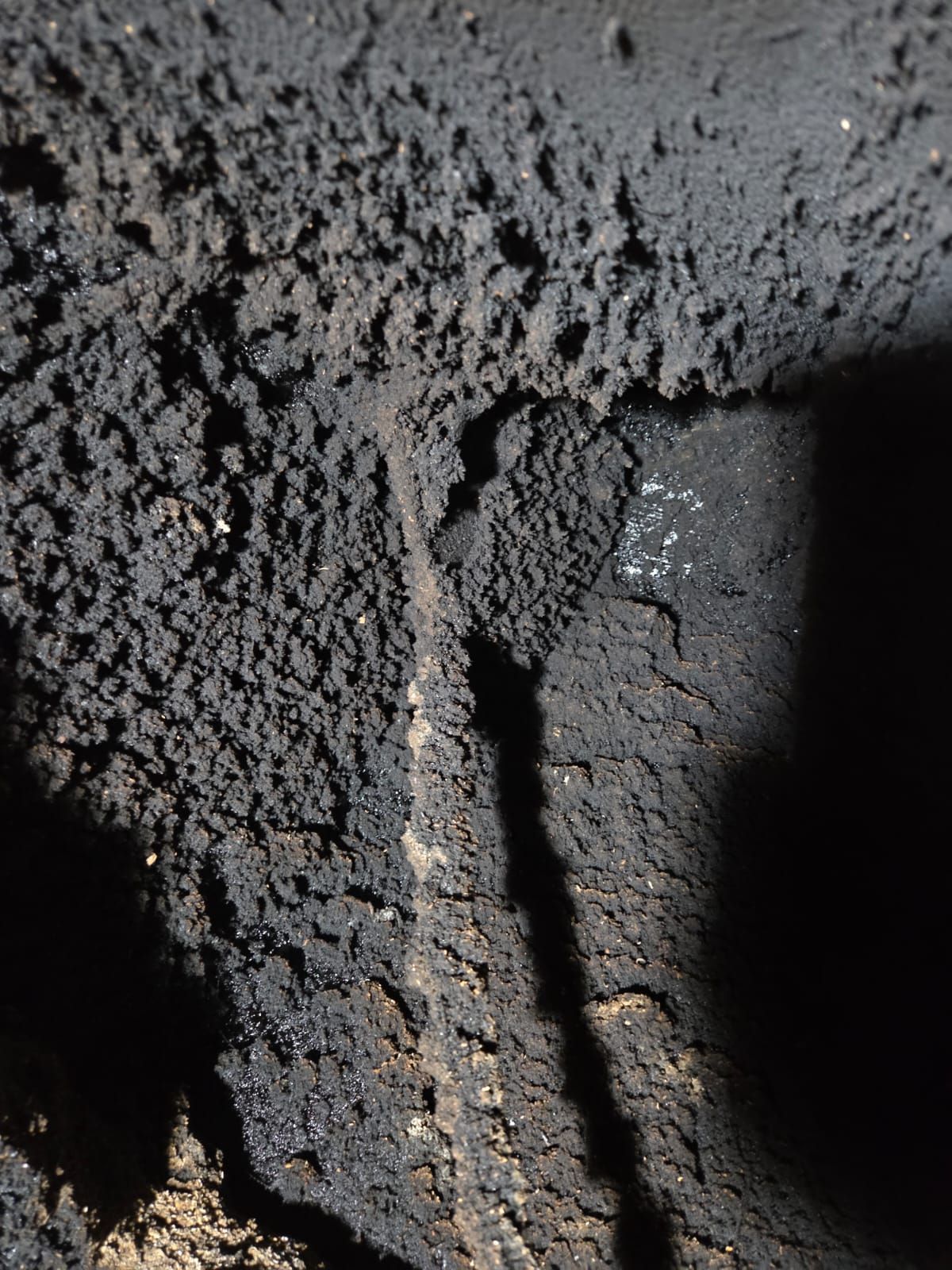 Primo piano dell'interno di un camino scuro e pieno di fuliggine. Depositi granulari e scagliosi ricoprono le pareti, con una linea verticale centrale.