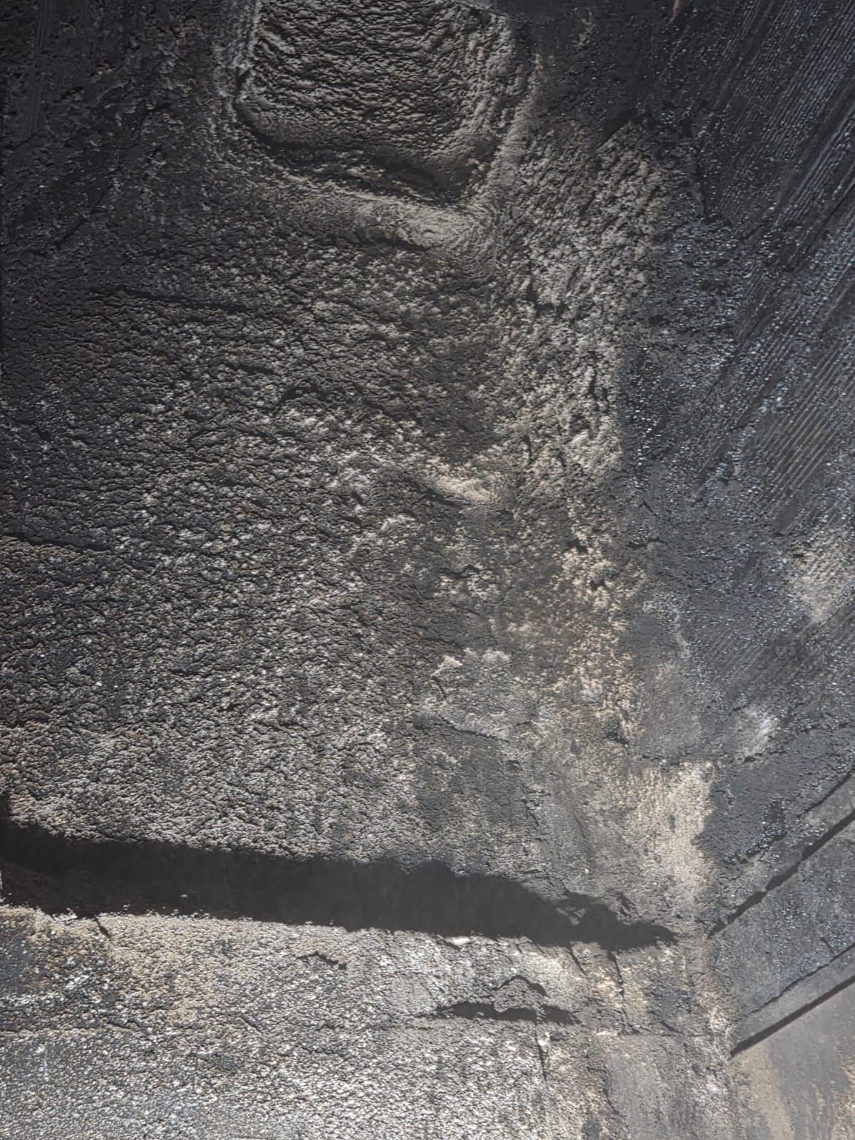 Superficie scura e ruvida, probabilmente pietra o asfalto, con una linea dritta e scura e una sezione di colore più chiaro.