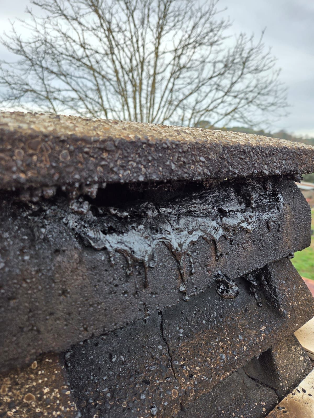 Primo piano della sommità di un camino in mattoni usurati, con residui scuri e fusi che cola lungo i lati.