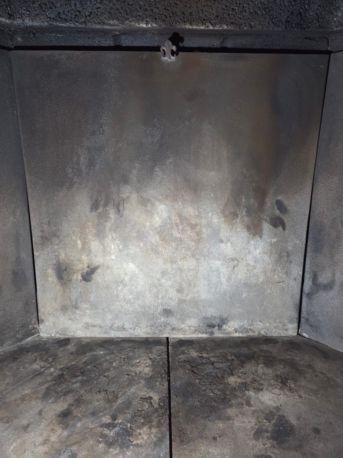 Interno di una stufa scura e sporca con un pannello posteriore in metallo e un chiavistello.