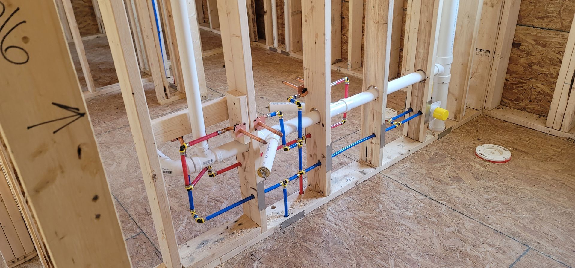 A bathroom in a house under construction with pipes coming out of the wall.