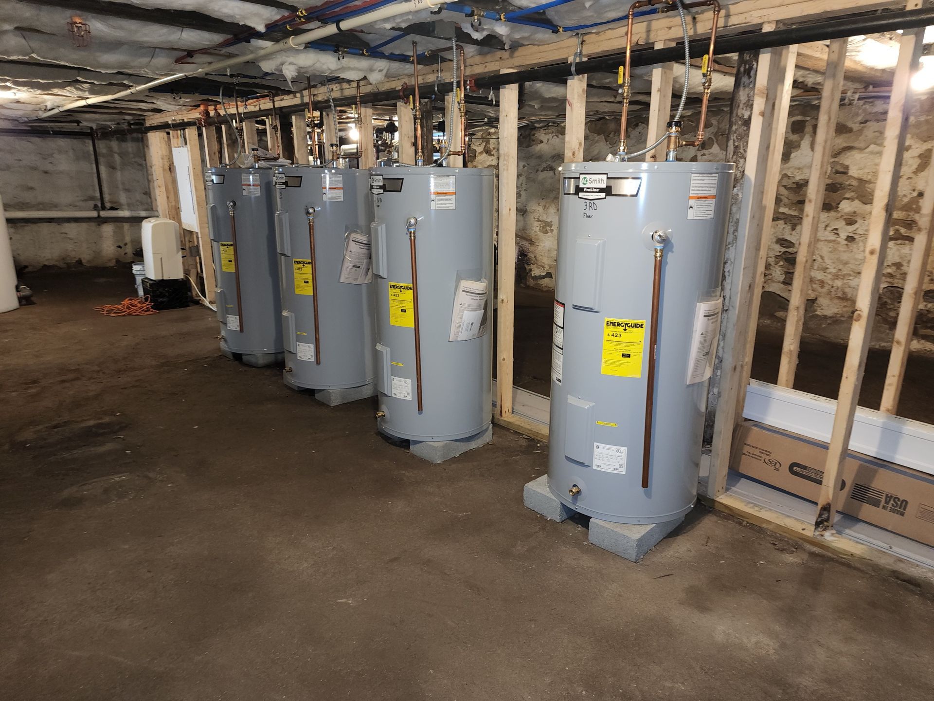 A row of water heaters are lined up in a basement.