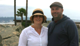 A man and a woman are posing for a picture and the woman is wearing a hat