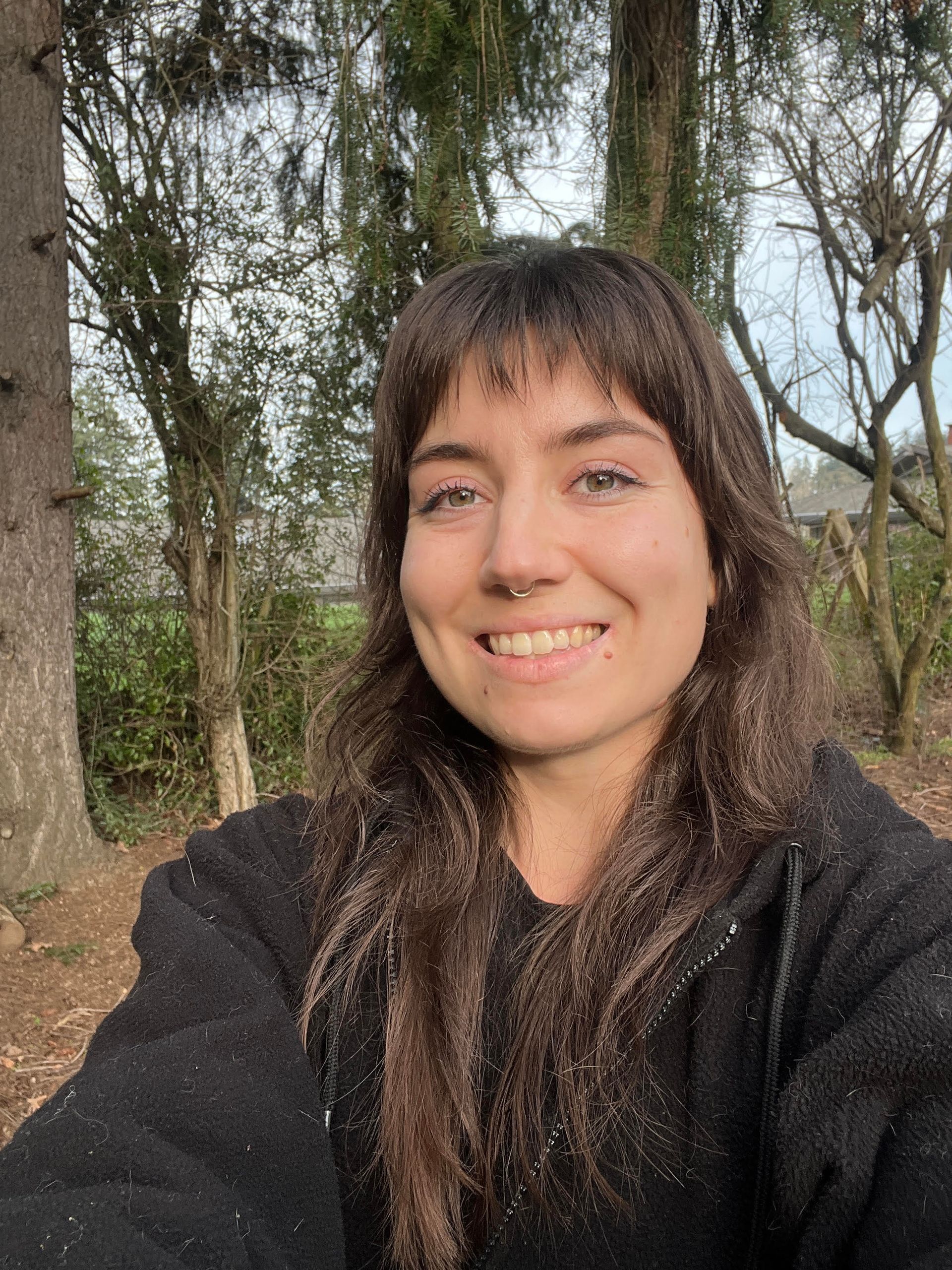 woman with long brown hair smiling with trees in the background