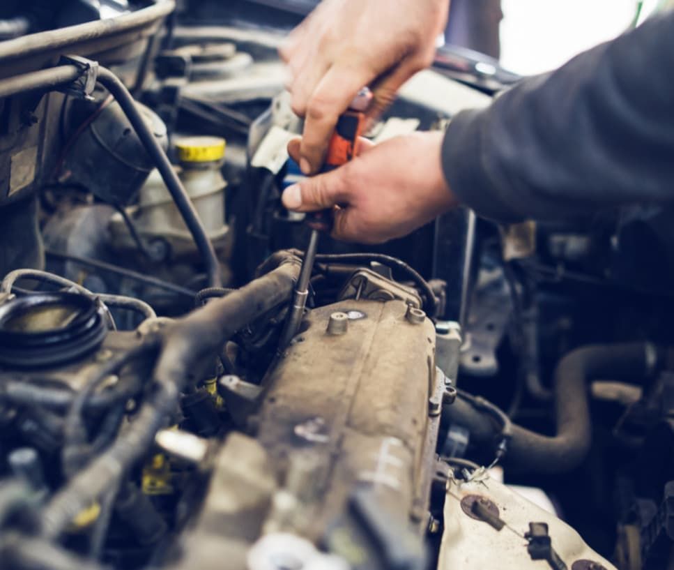 A Man Is Working On A Car Engine With A Screwdriver — Uncle Tonys Auto And Mechanical In Currumbin Waters, QLD