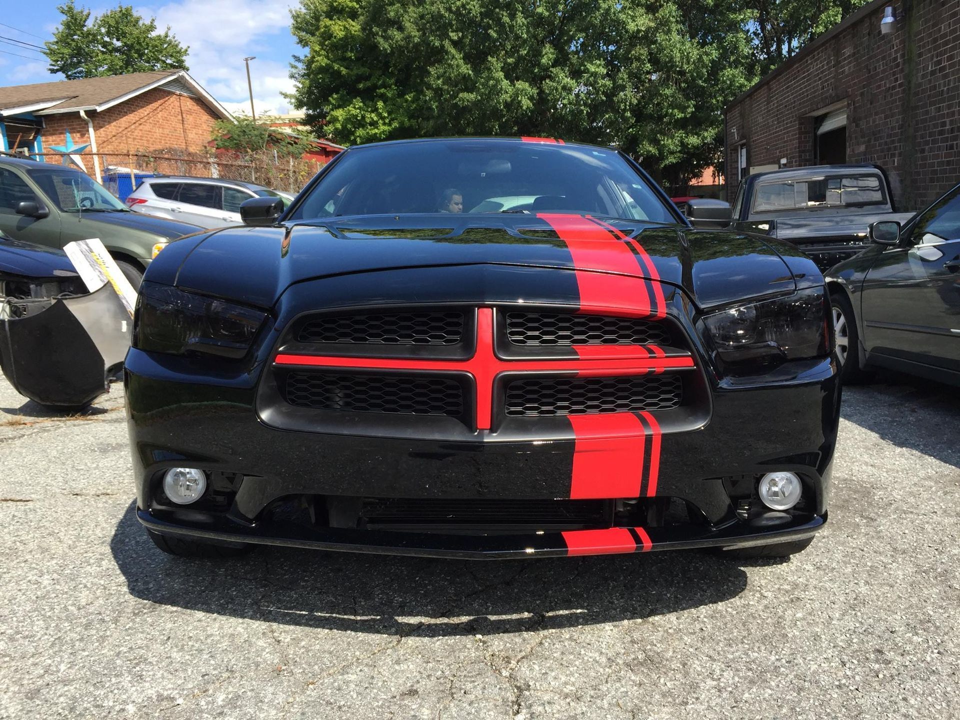 Black Dodge Charger with red racing stripes parked outside on a sunny day.