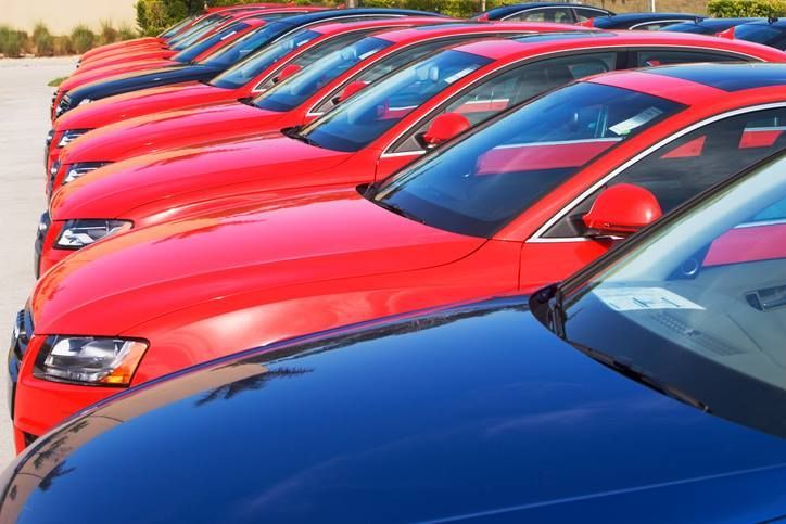 Cars parked in a row; red and blue vehicles, sunny outdoor setting.