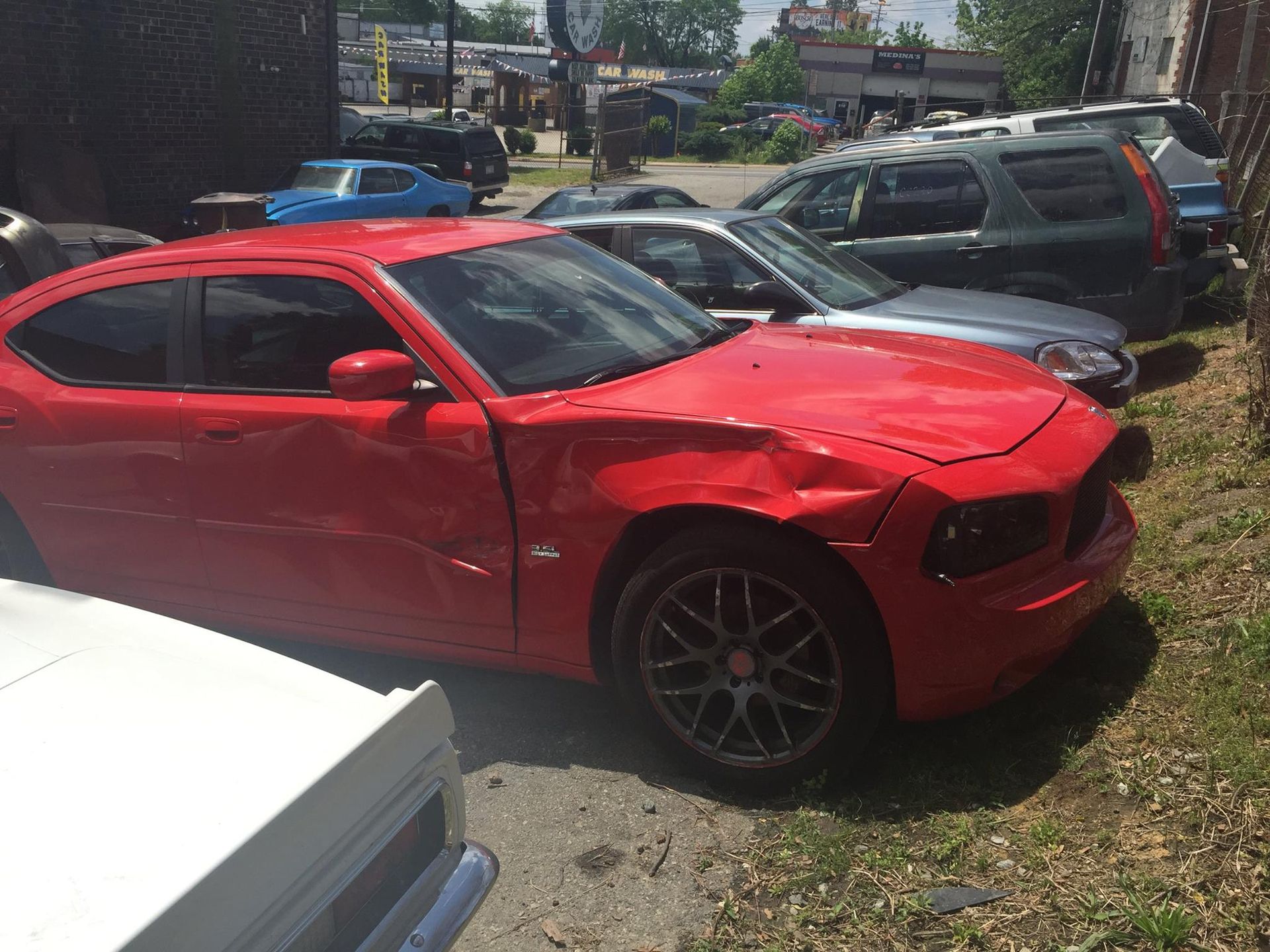 Red Dodge Charger with significant front-end damage parked in a lot with other vehicles.