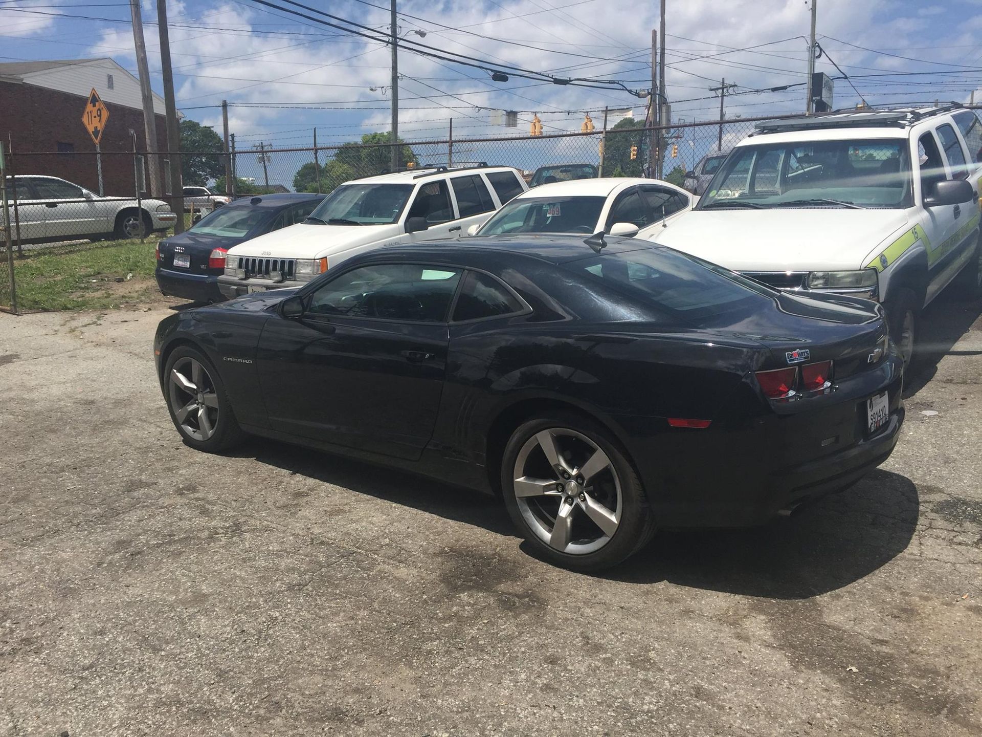 Black Chevrolet Camaro parked in a lot with other vehicles on a sunny day.