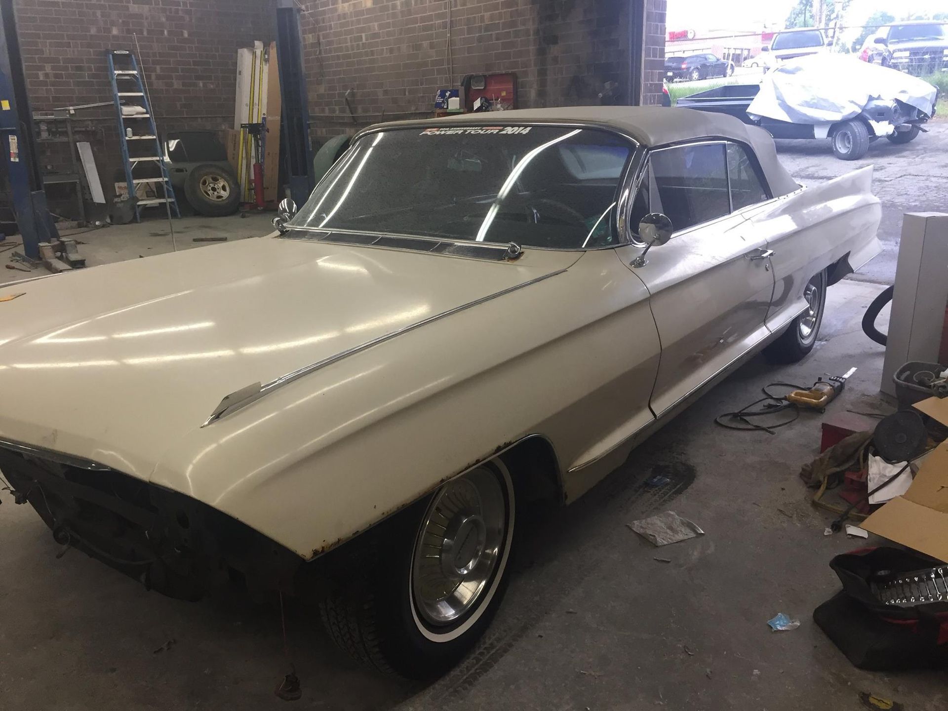 White vintage convertible car in a repair shop with the top down.
