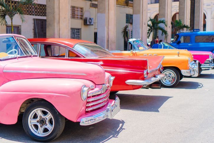 Rows of colorful vintage cars parked in front of a light-colored building in Cuba.