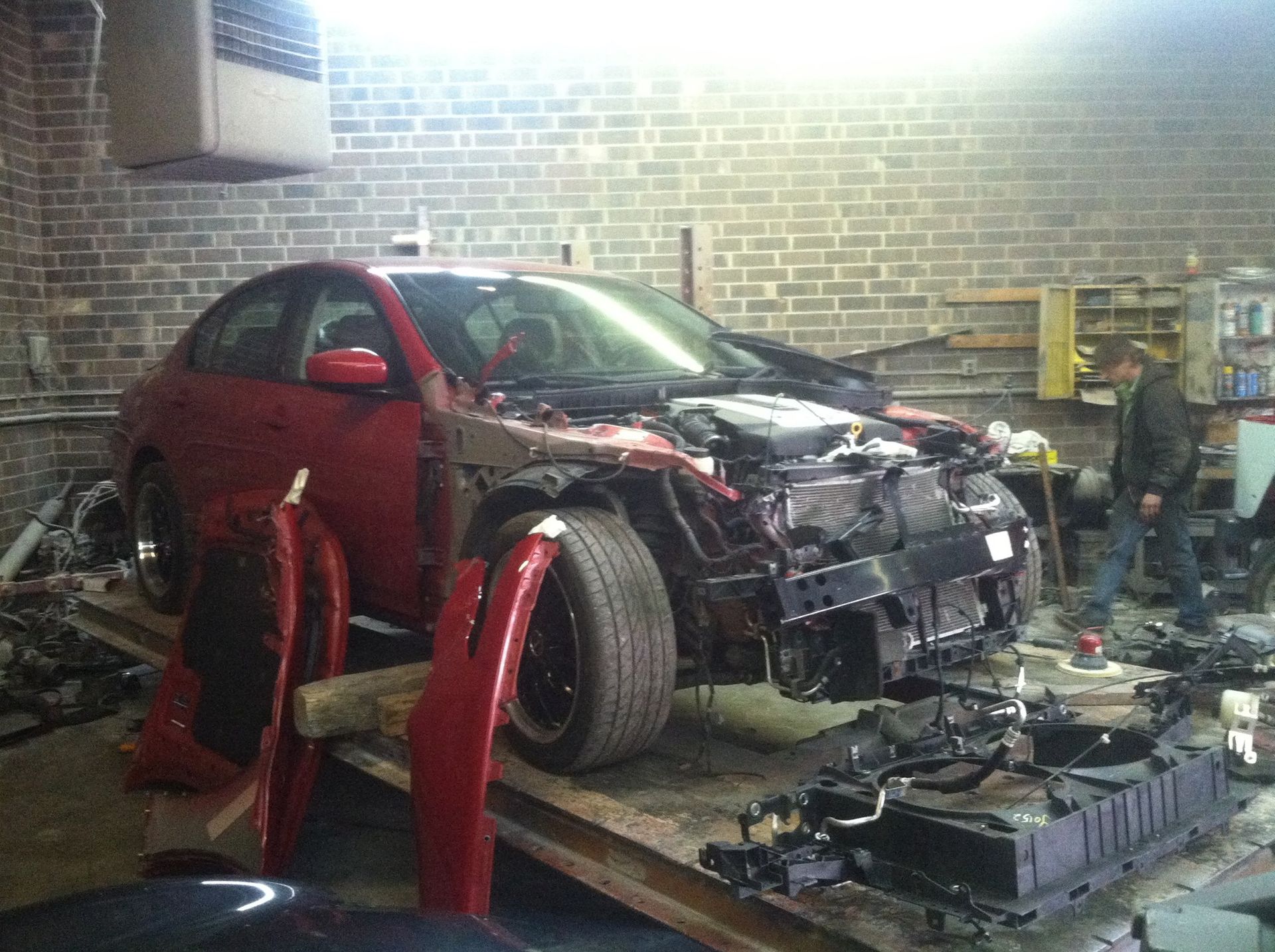 Red car in garage, partially disassembled for repair, person works nearby.