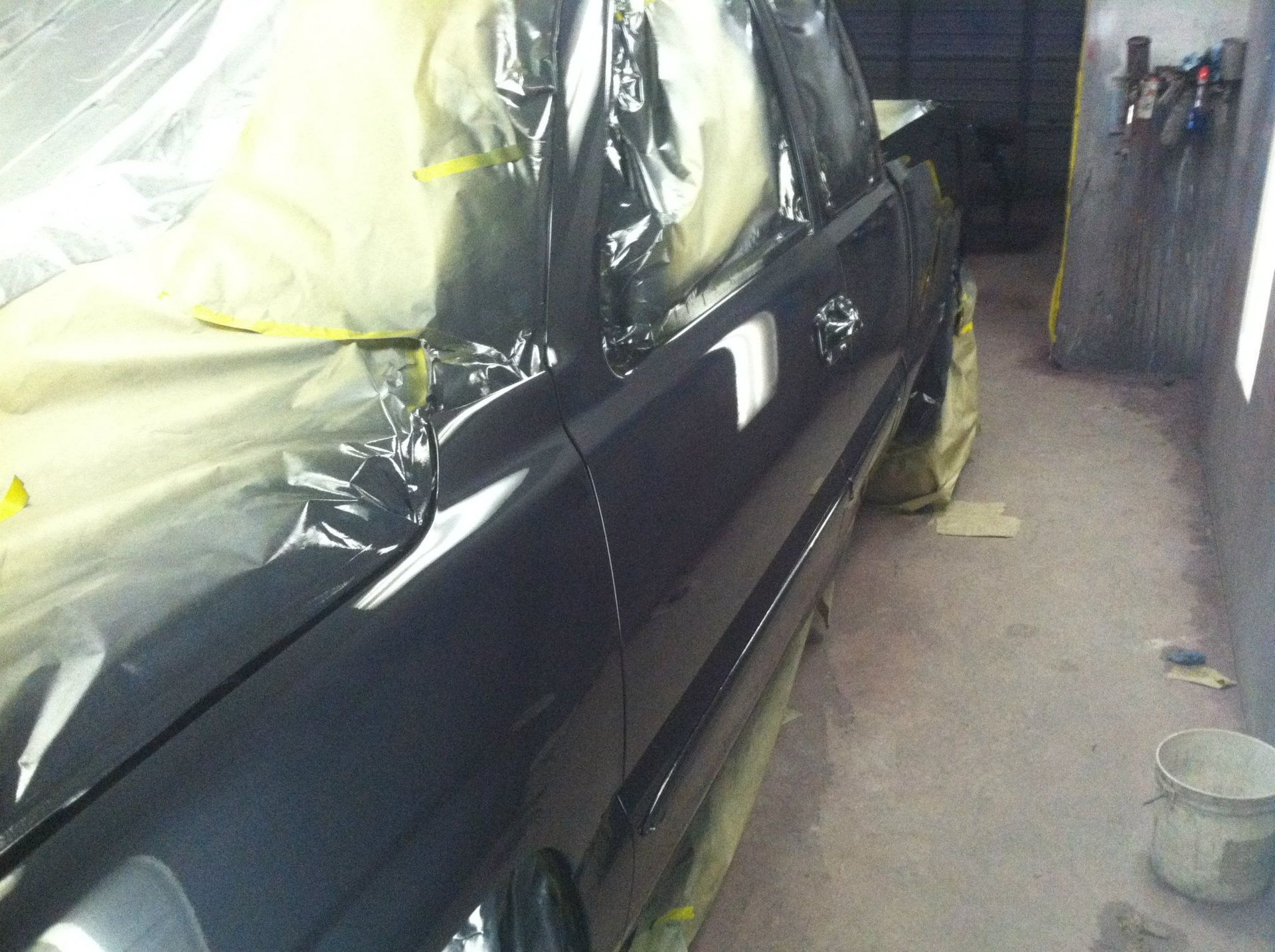 Car door being painted, taped and covered in a garage.
