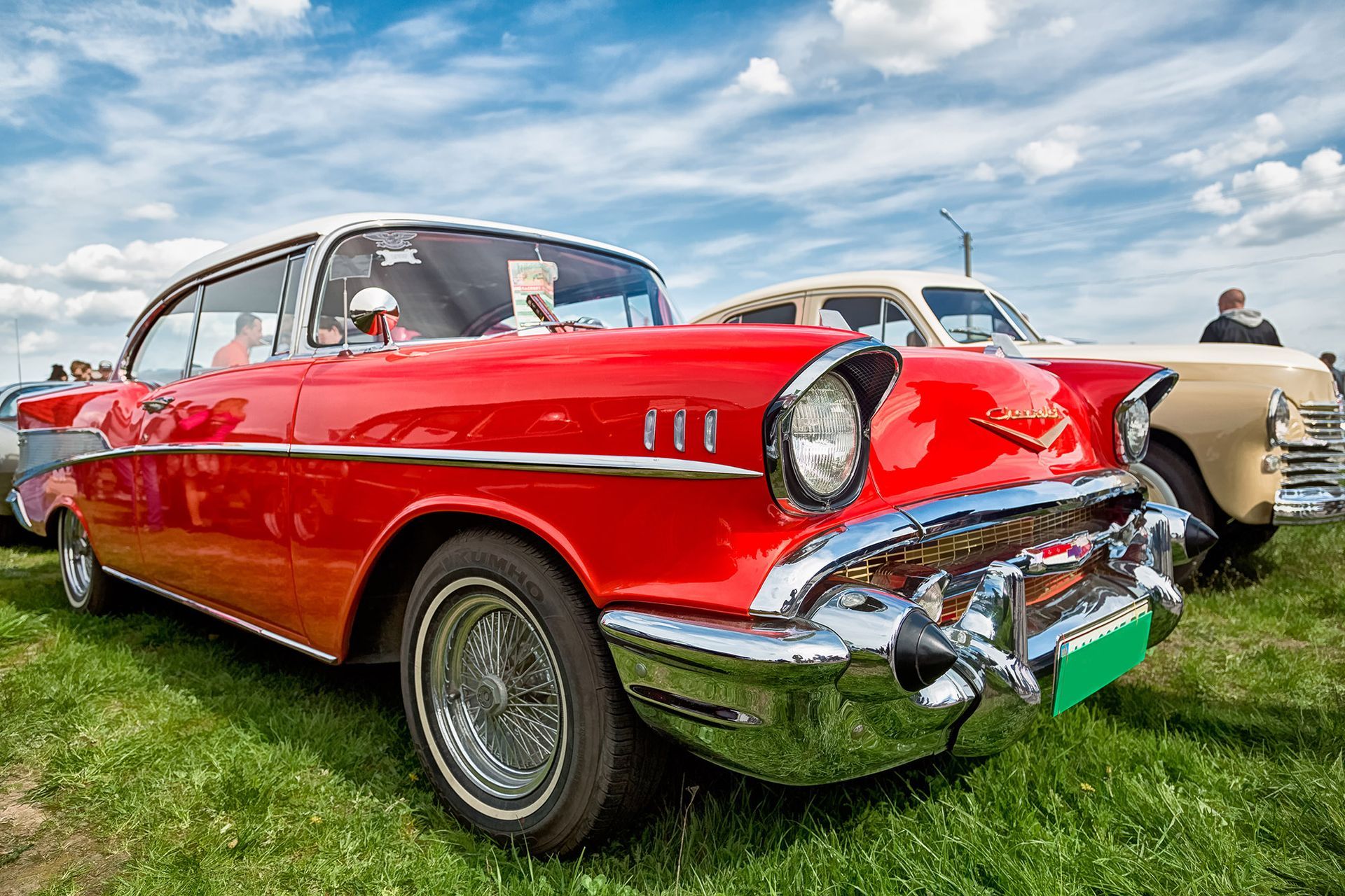 Red classic Chevrolet car on display at an outdoor car show, chrome detailing, white roof.