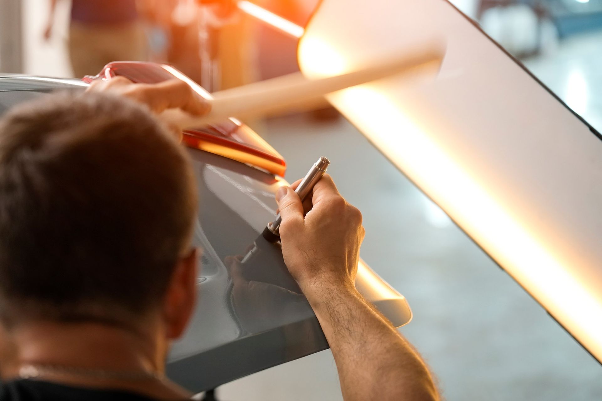 A person using a tool on a car body panel under bright lights, likely dent removal.