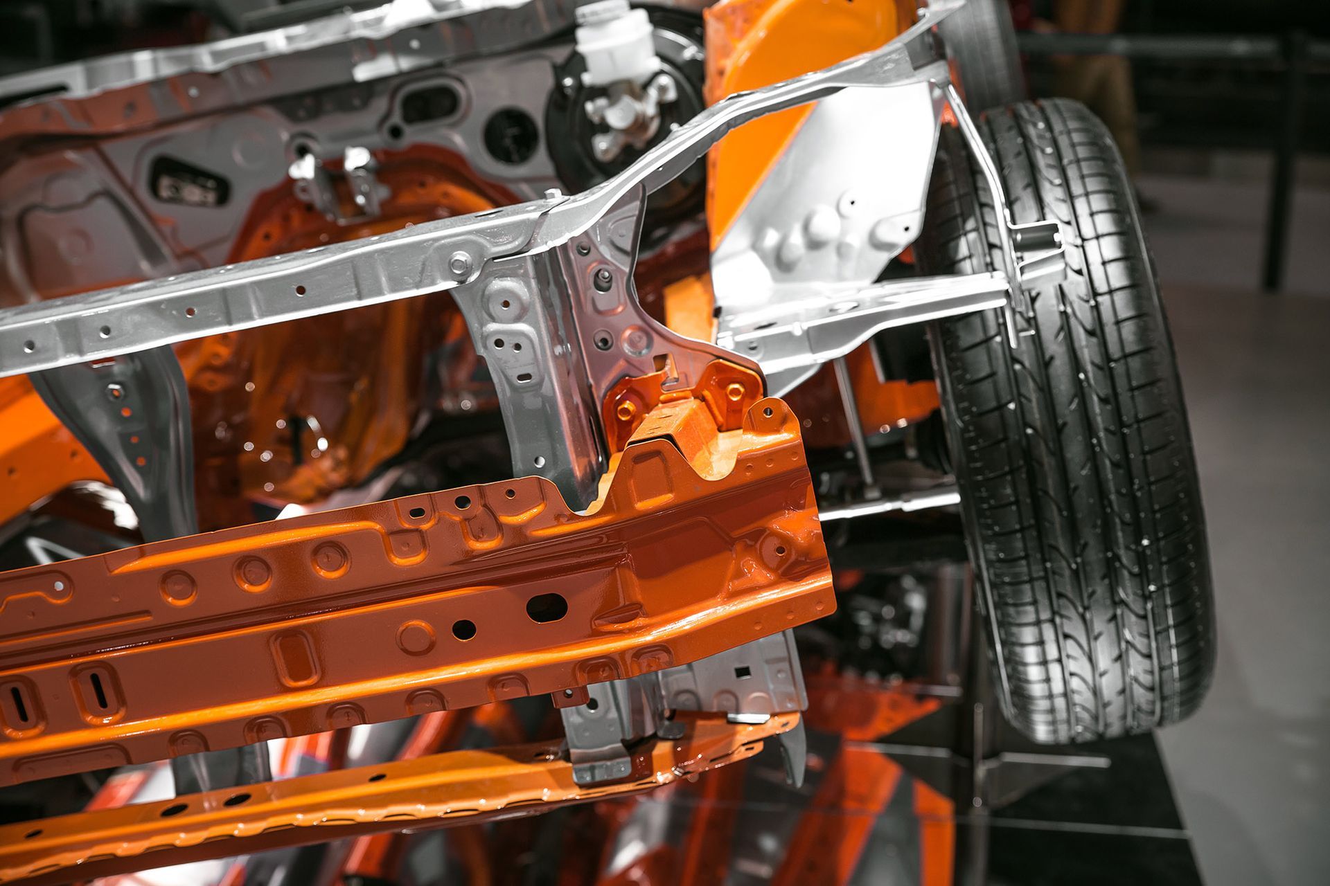 Orange and silver car chassis with a tire attached, showcasing structural components.