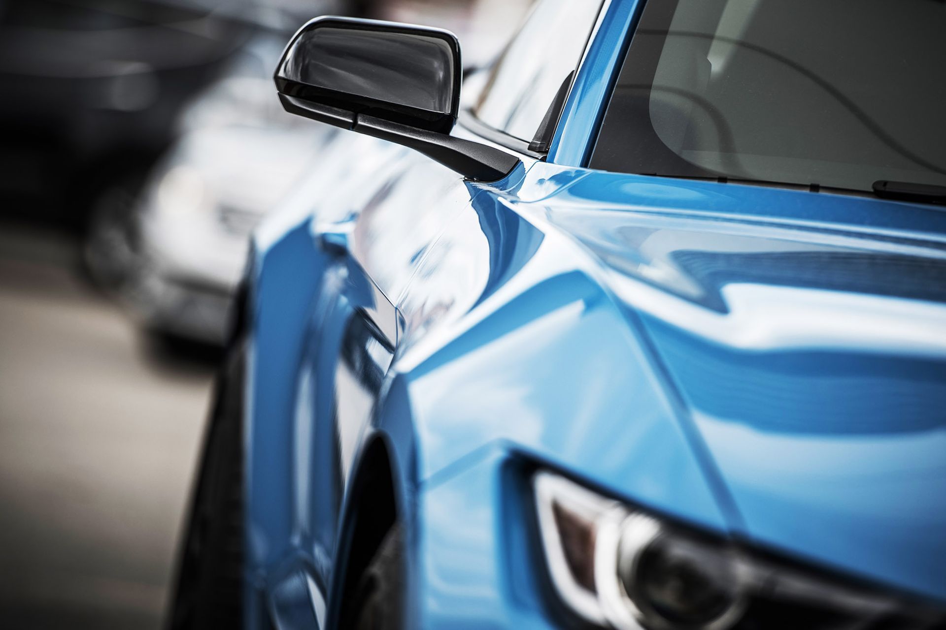 Blue sports car's front quarter, side mirror visible, other cars blurred in background.