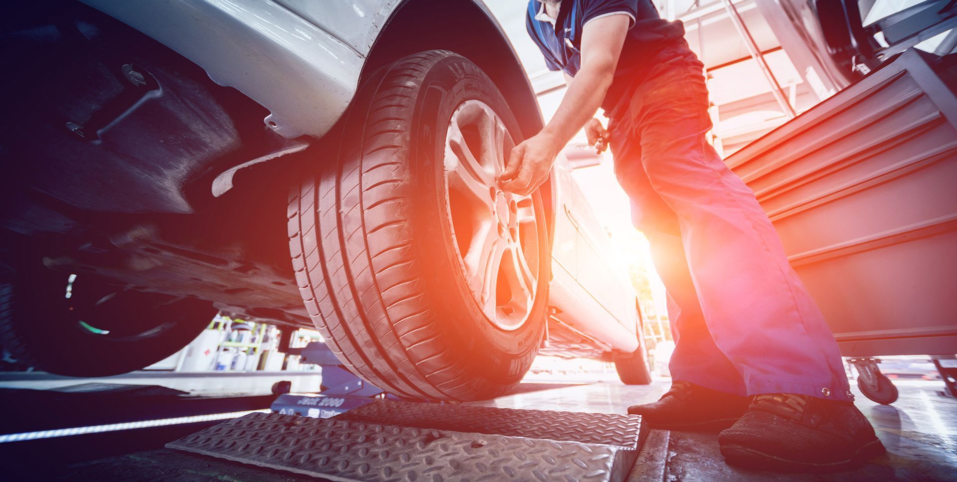 Mechanic replacing a car tire in a garage, using a wrench. Bright sunlight.