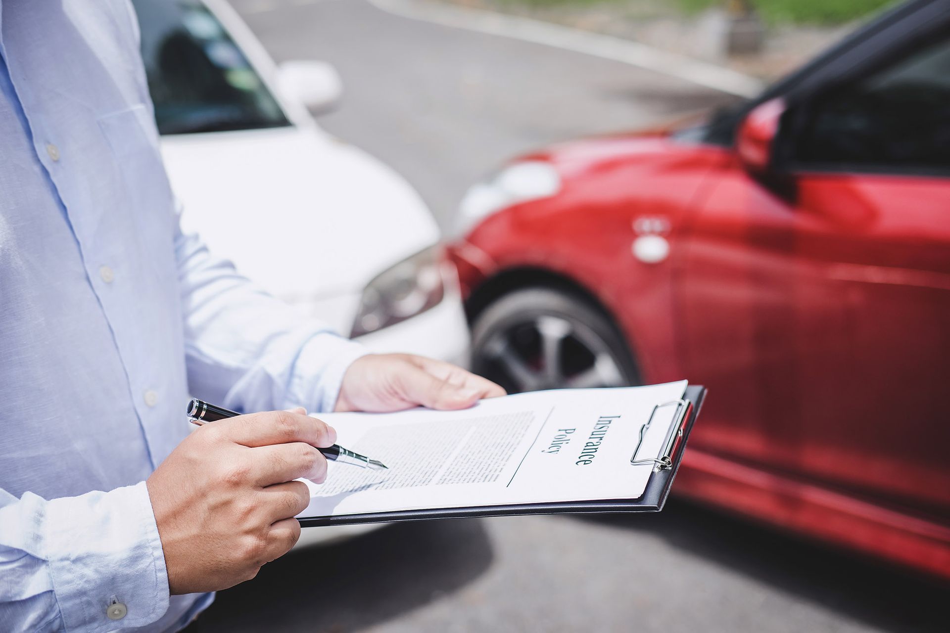 Person with clipboard inspecting car accident damage involving a red and white car.