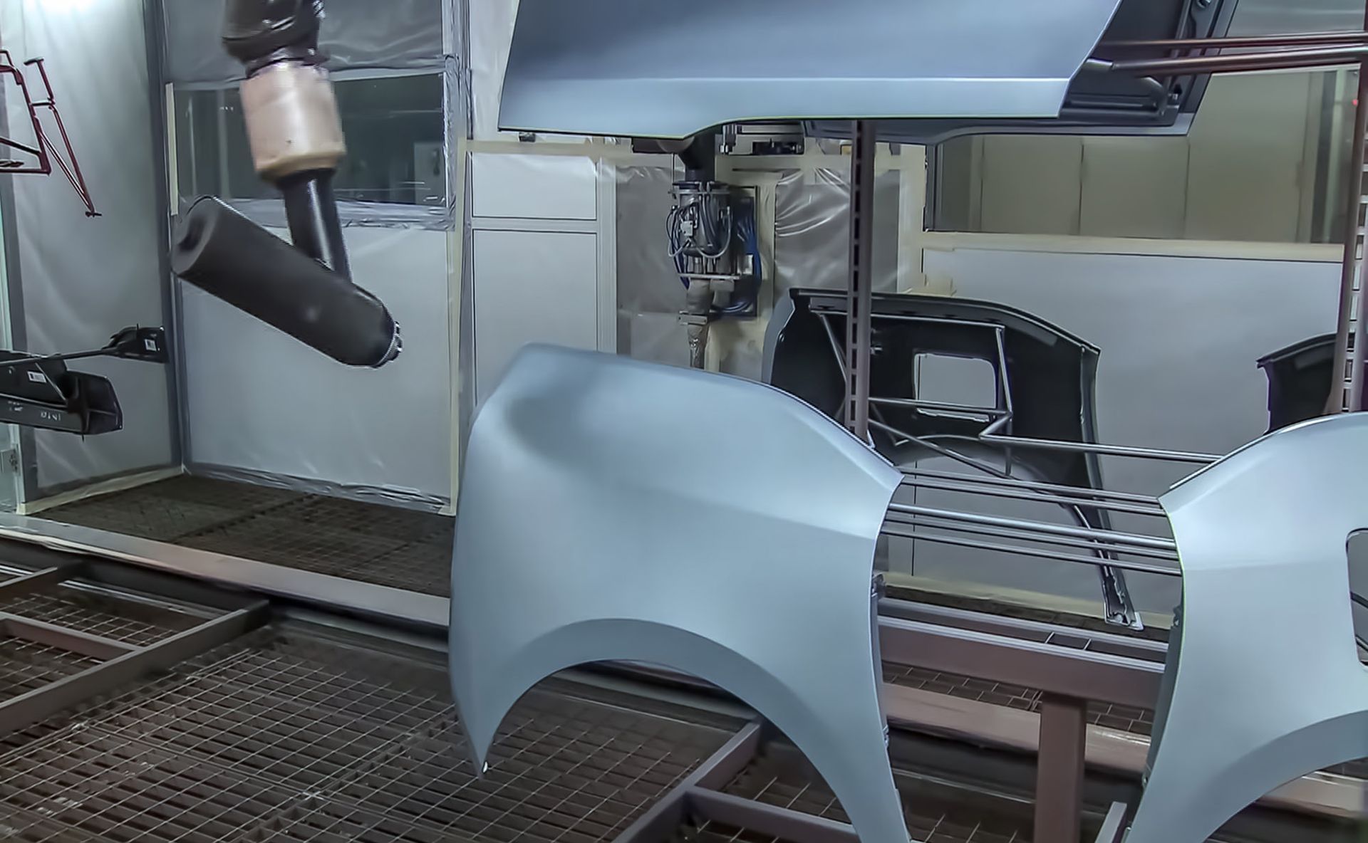 Car parts hanging in a paint booth being sprayed with light blue paint.