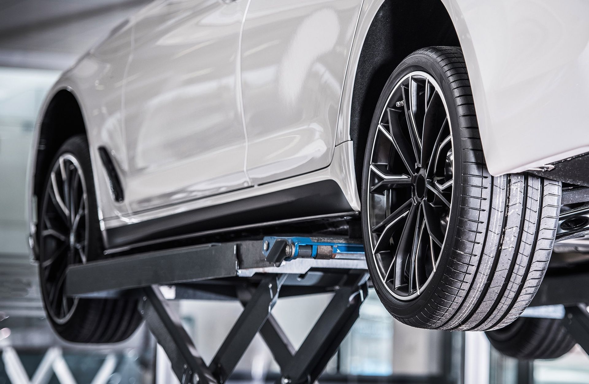 White car on a hydraulic lift in a garage, showcasing the undercarriage and wheels.