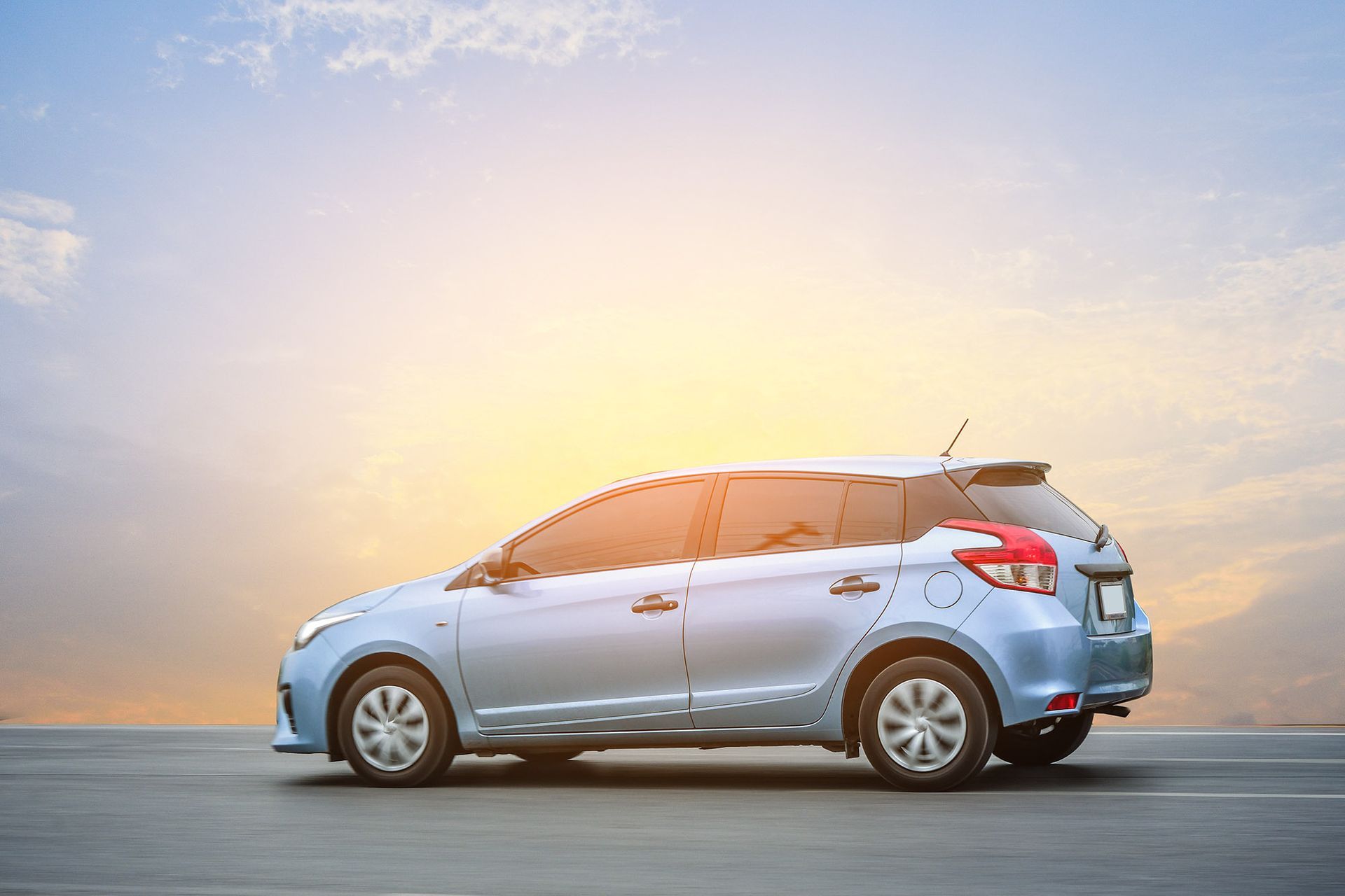 Blue car parked on asphalt, bright sky in the background.