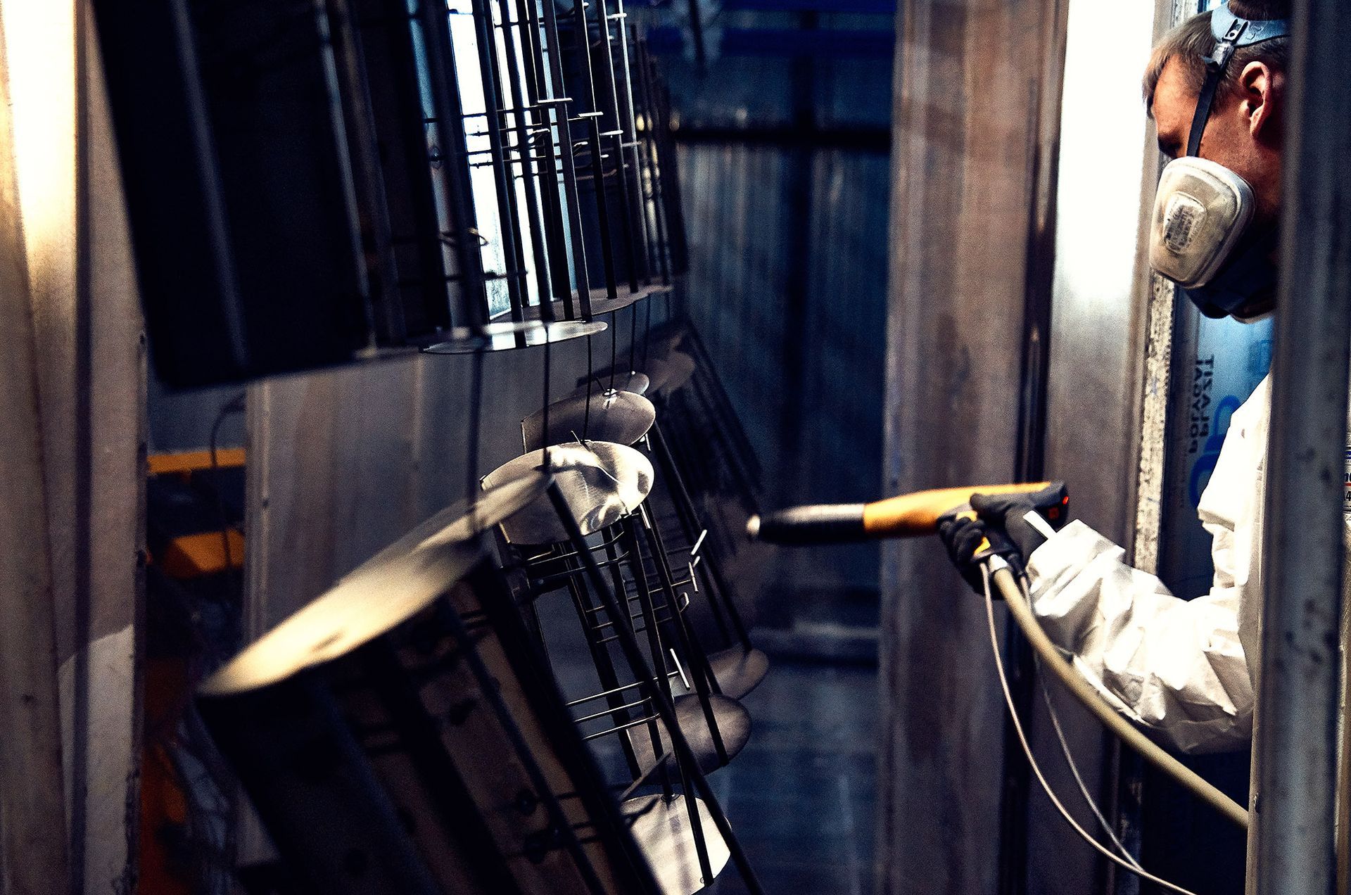 Man in protective gear powder coating metal furniture in a factory.