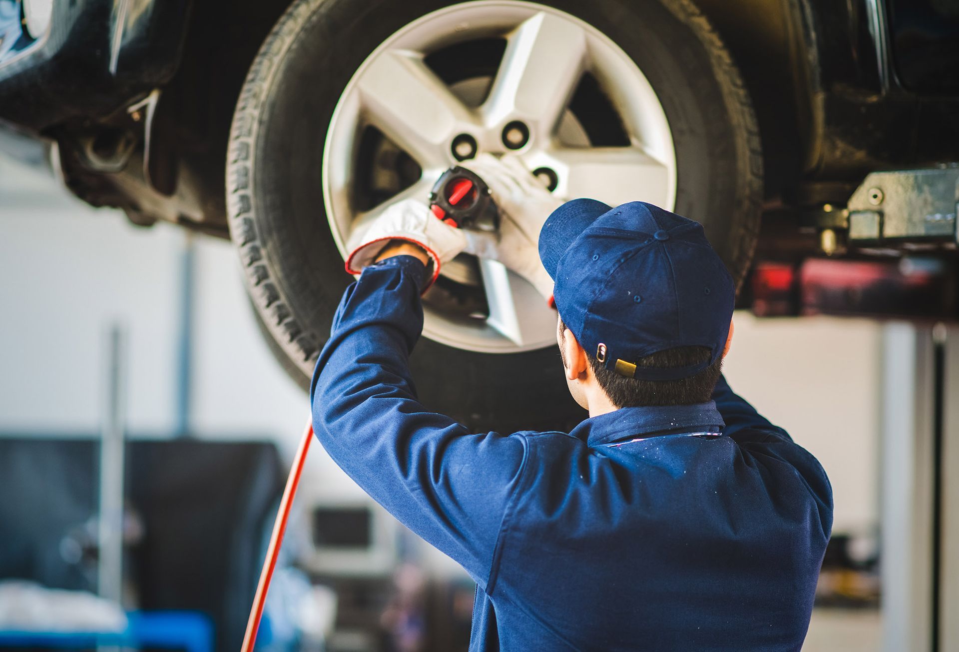 Mechanic in blue uniform uses a wrench to tighten a car's wheel, indoors.