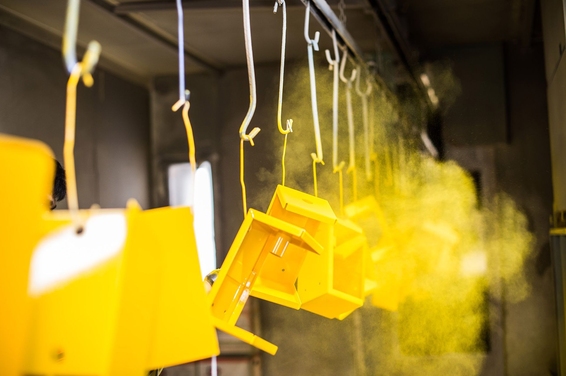 Yellow powder coating applied to metal boxes hanging from hooks in a factory.