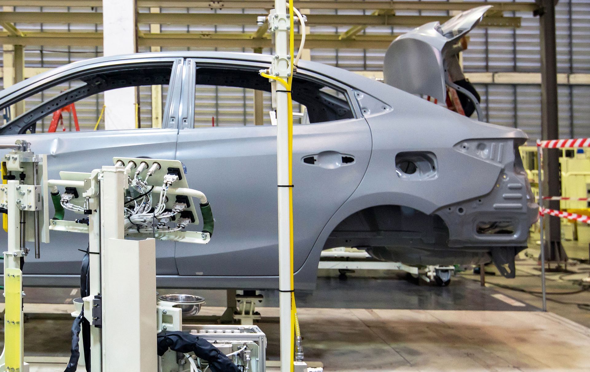 Car body on an assembly line, gray metal, open doors and trunk, factory setting.