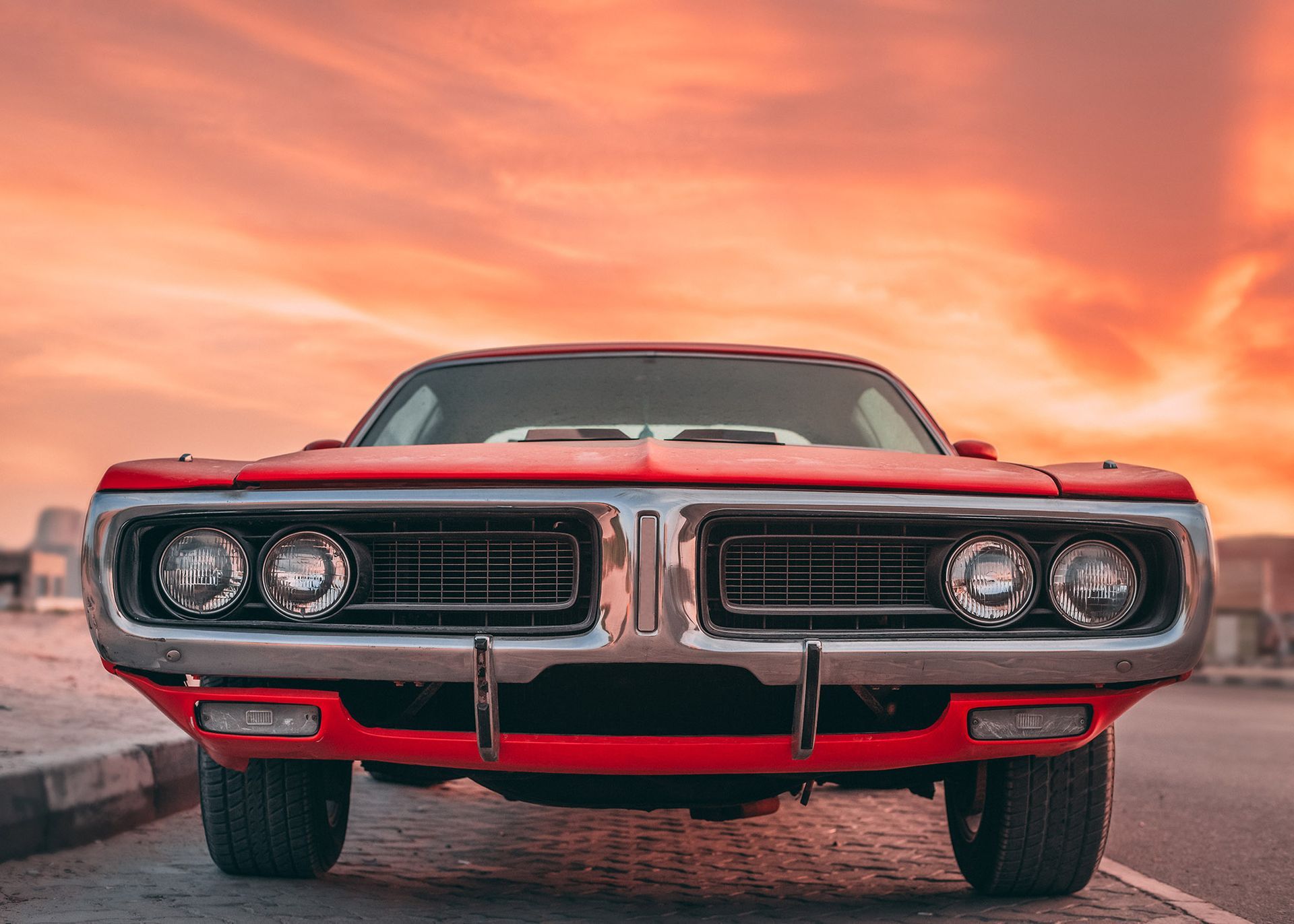Red classic car, front view, set against an orange sunset sky.