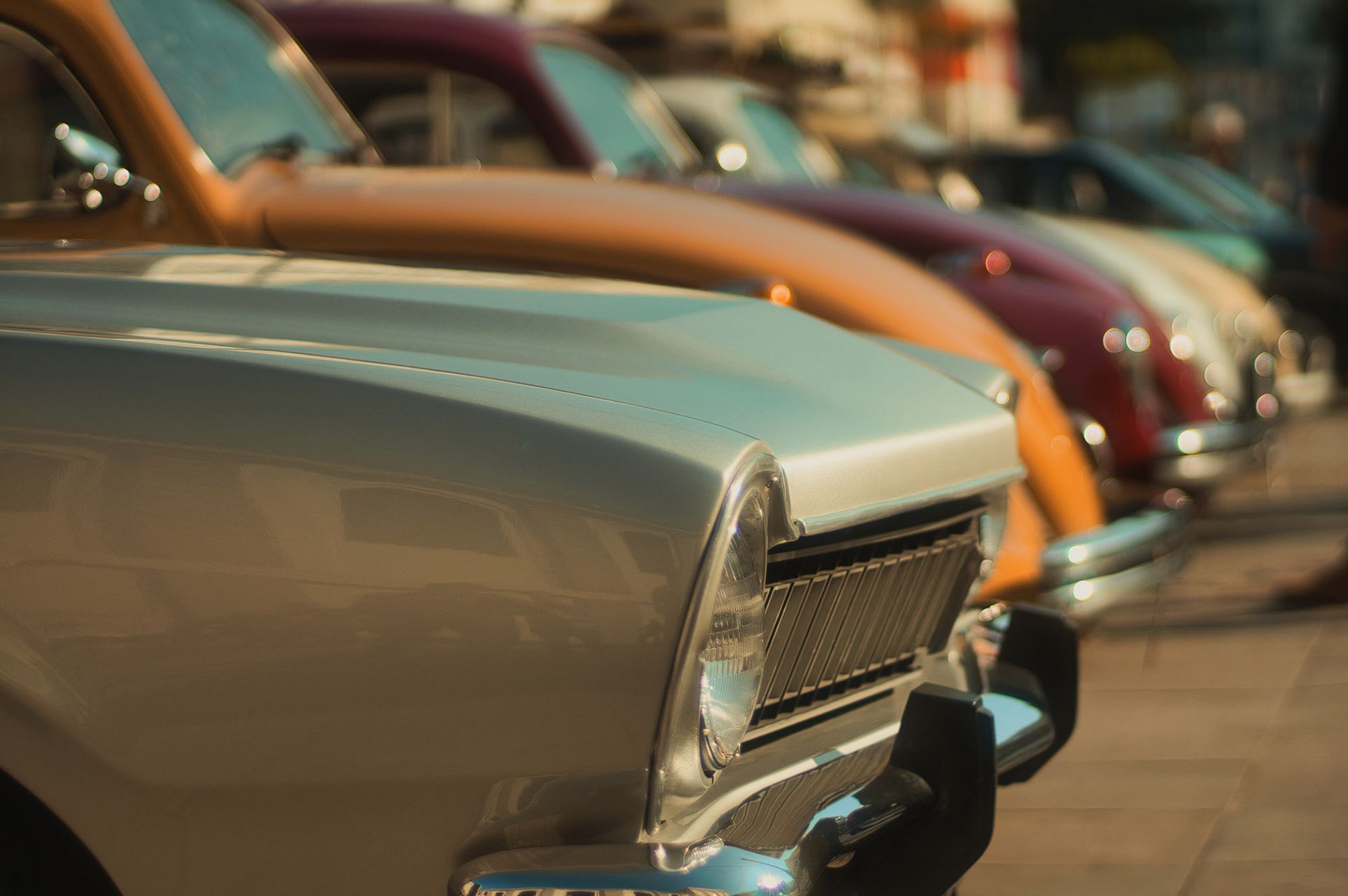 Row of vintage cars parked in a row, close-up on silver hood, others in orange, red, and green.