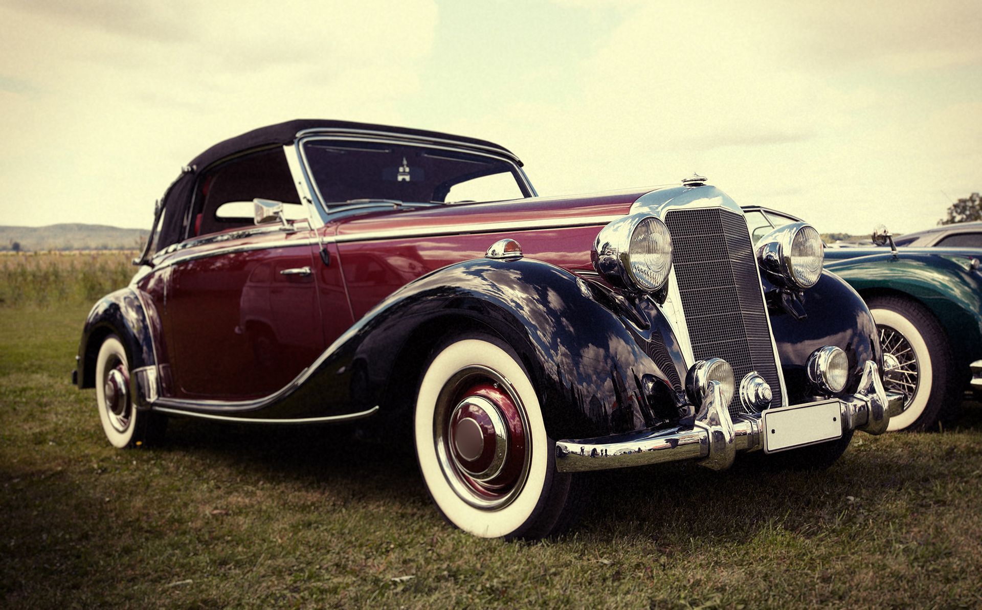 Classic maroon and black convertible car with white tires on grass.