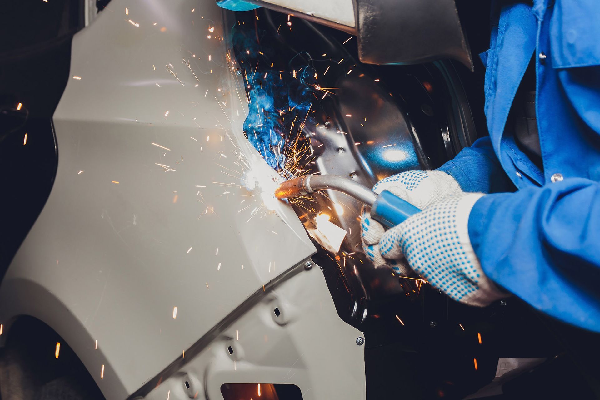 Person welding car panel, sparks flying.
