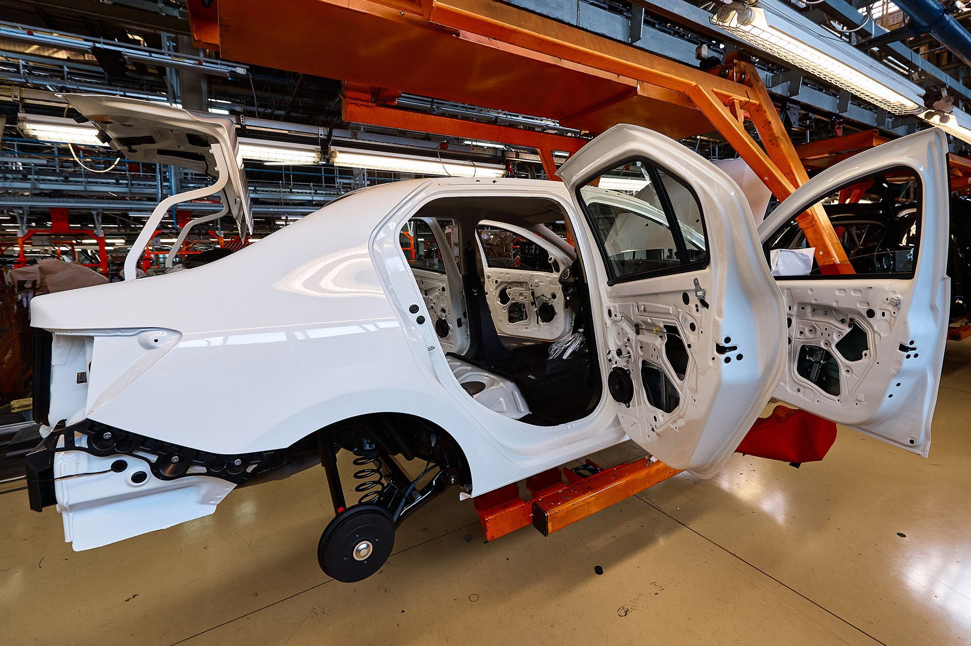 White car frame on an assembly line with doors open, in a factory setting.