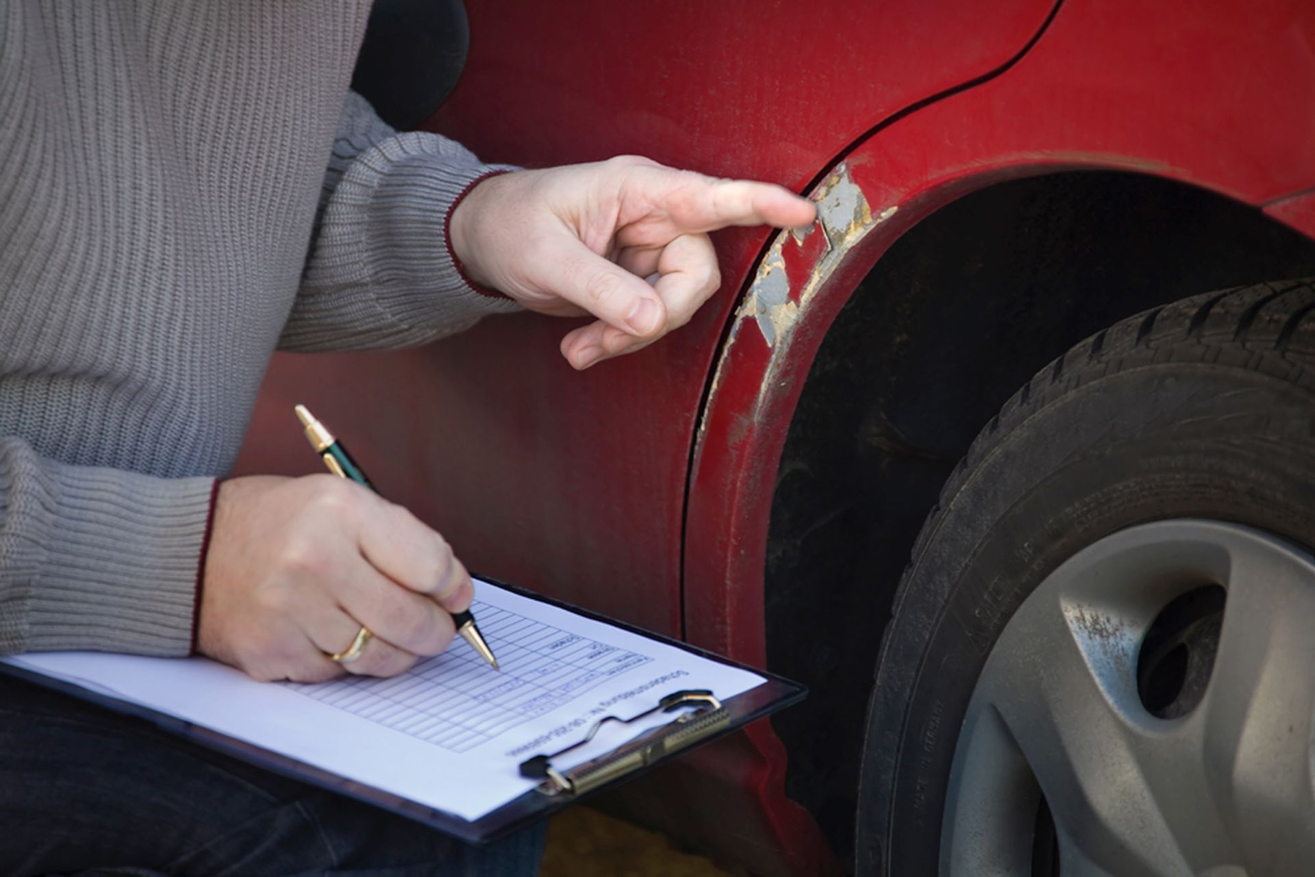 Person inspecting car damage, pointing at paint scratches and writing on a clipboard.