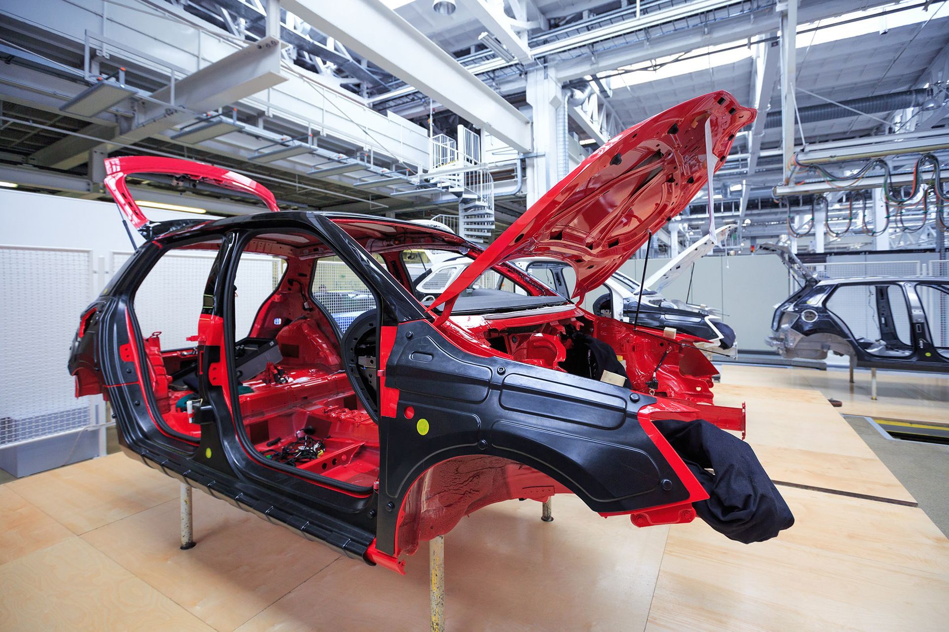 Car frame in a factory, doors open, red interior, black exterior panels, overhead lighting.