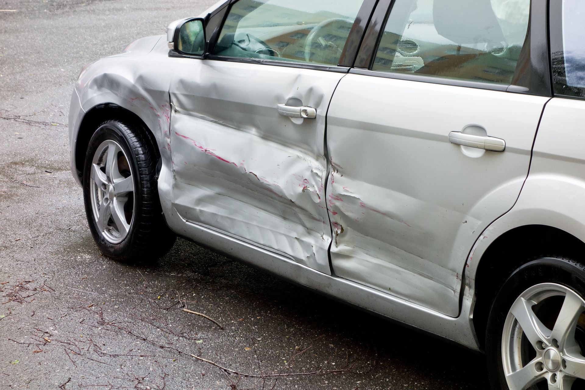 Silver car with significant damage to the driver's side doors.