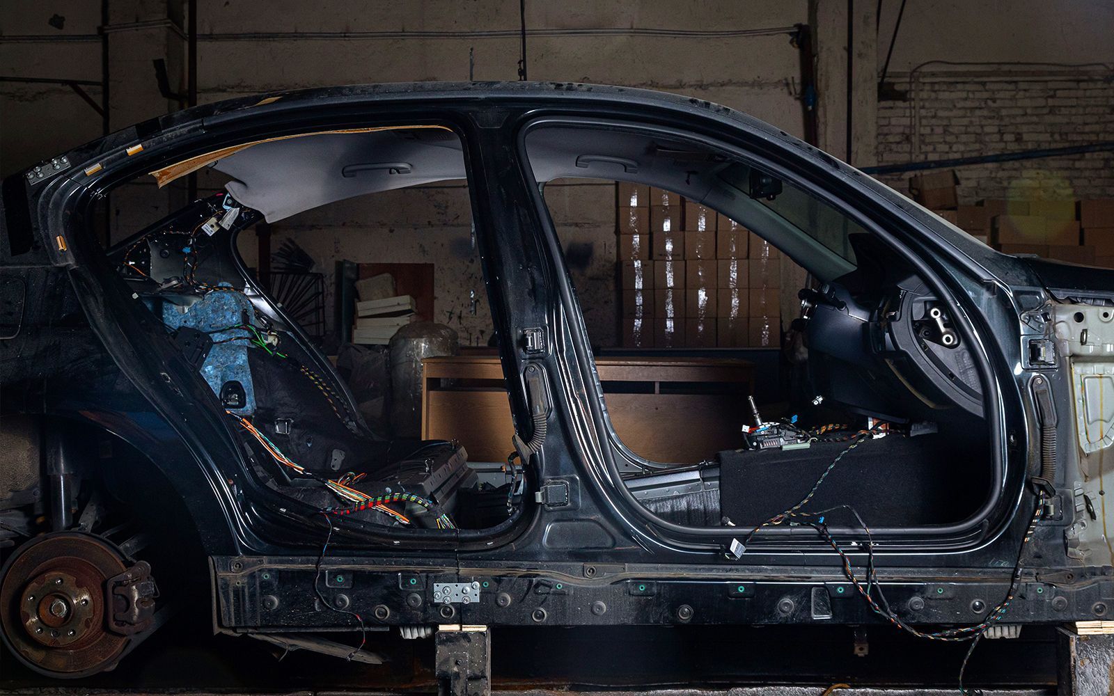 Stripped-down black car chassis in a workshop, revealing interior structure, wiring, and a wheel.