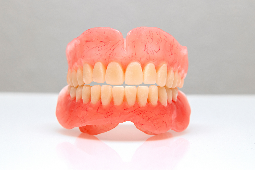 Dentures with light peach gums and beige teeth sit on a white surface.
