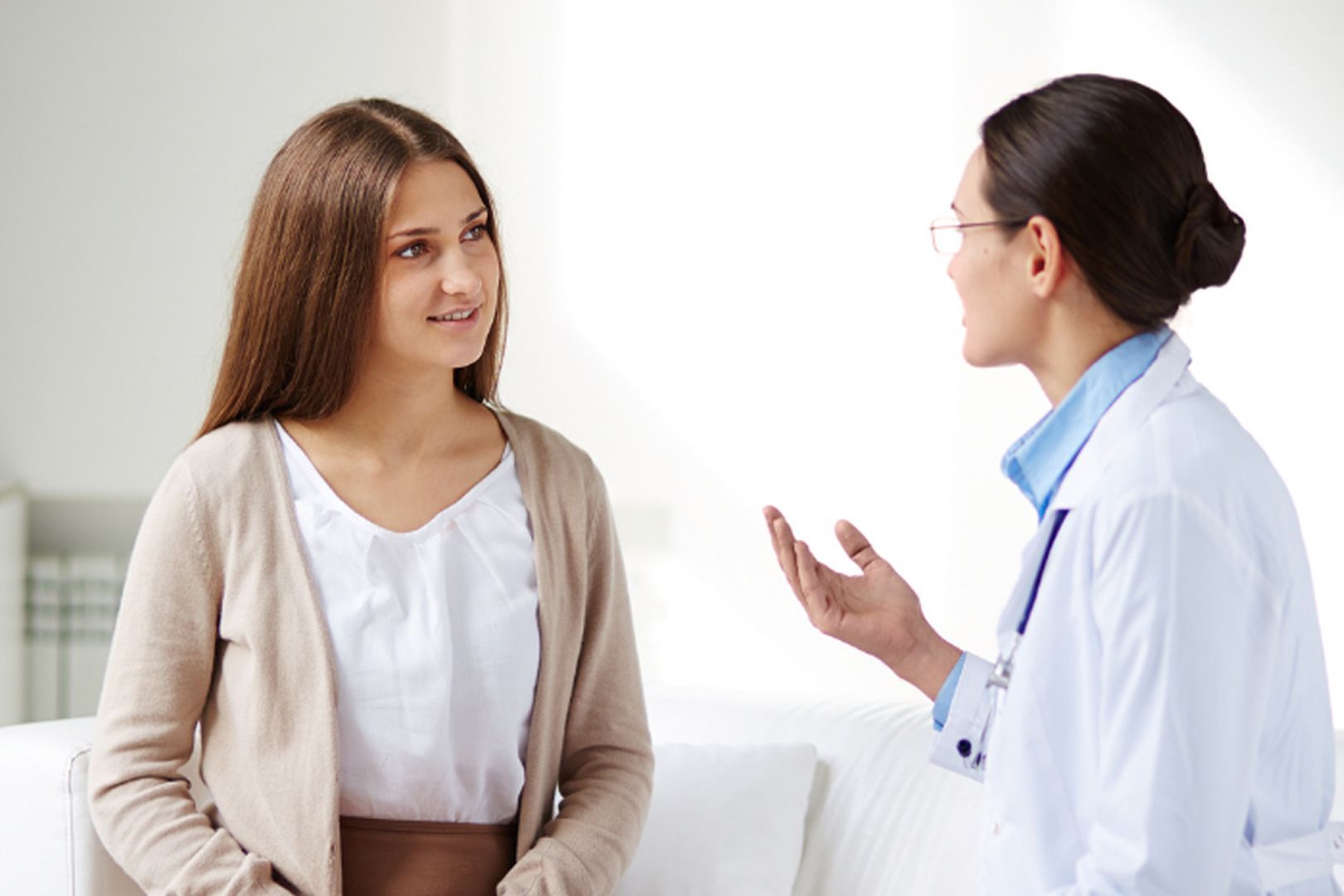 Woman in cardigan talking with a doctor wearing a white coat in an office setting.
