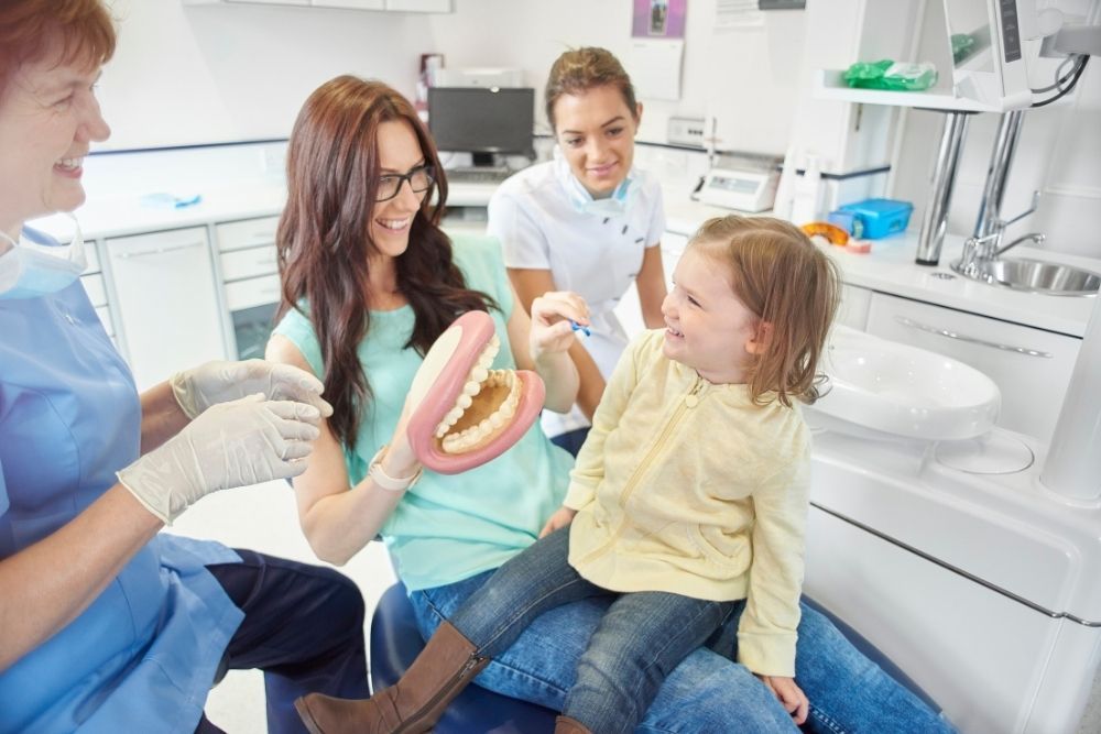 Woman and child in dental office, looking at model teeth with dentist and assistant.