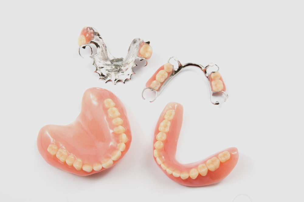 Four sets of dentures laid out on a white surface; pink gums with yellow teeth, some with metal clasps.