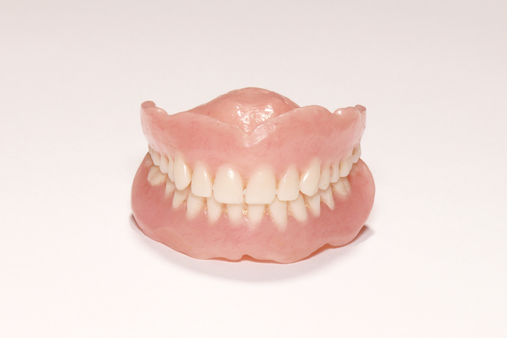Full set of dentures, pink gum and white teeth, sitting on a white surface.