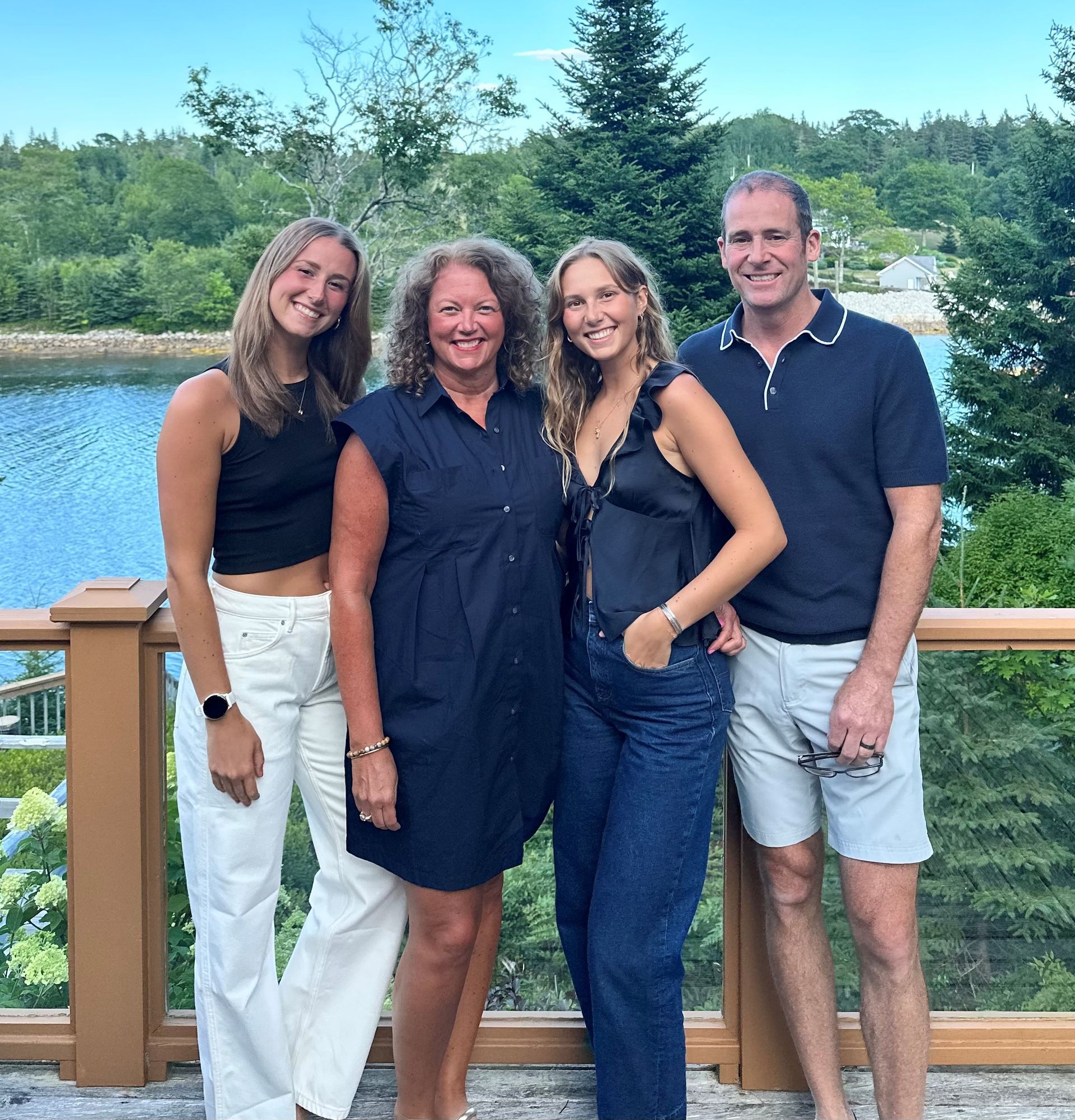 Family of four poses on a deck overlooking water; two young women, a woman, and a man.